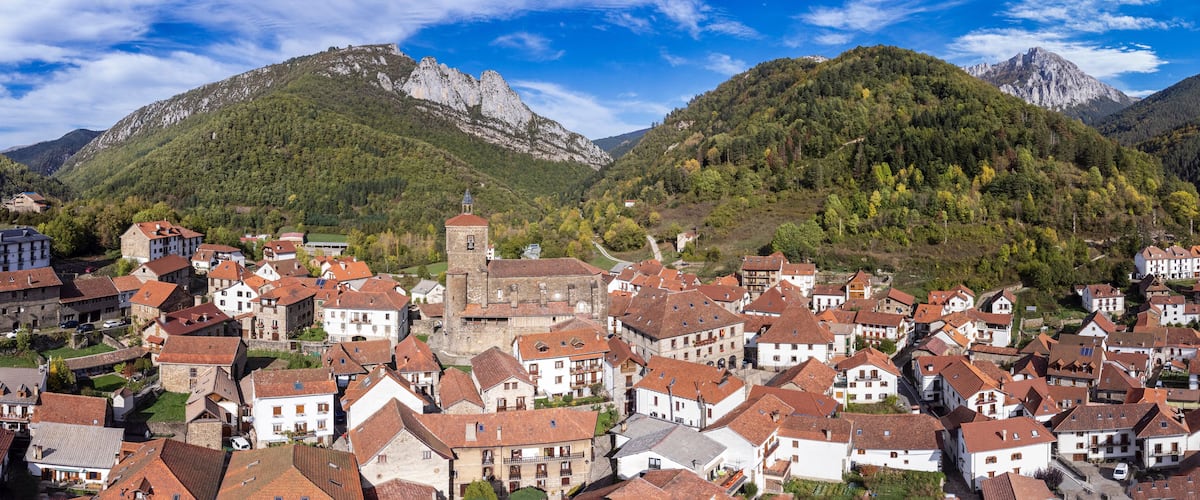 A mountainous town with red-roofed buildings, a prominent church, and lush green hills.