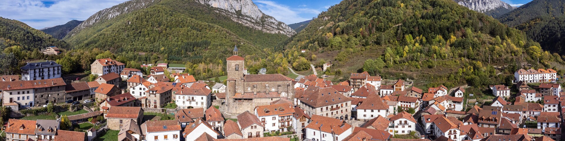 A mountainous town with red-roofed buildings, a prominent church, and lush green hills.