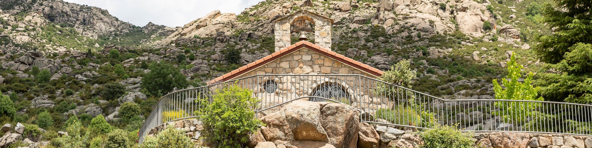 Uma capela de pedra com telhado vermelho, rodeada por terreno rochoso e vegetação.