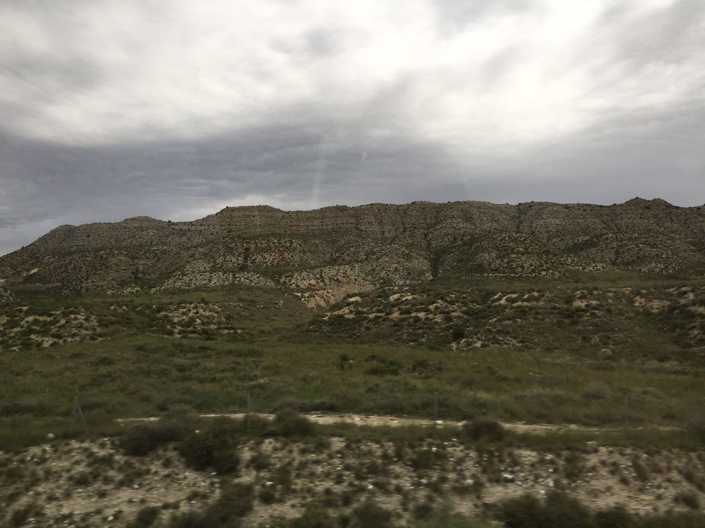 A rugged mountain range with sparse vegetation under a cloudy sky.