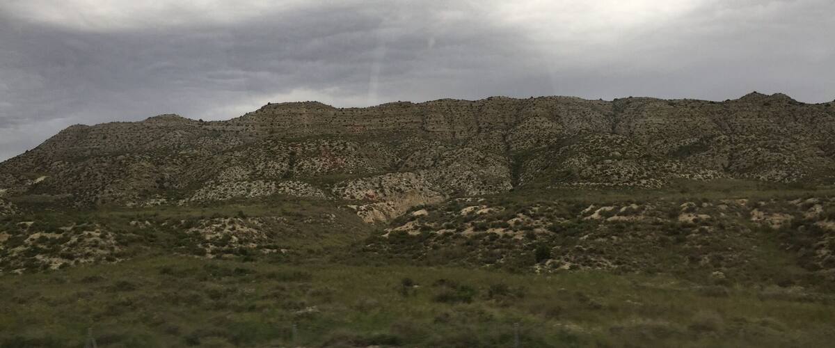 A rugged mountain range with sparse vegetation under a cloudy sky.