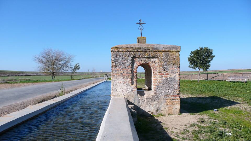 A narrow water channel with a brick structure featuring an archway and a weather vane on top.