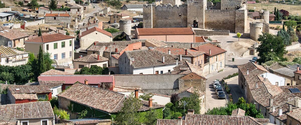 A historic town with stone buildings, a prominent castle, and rolling hills in the background.