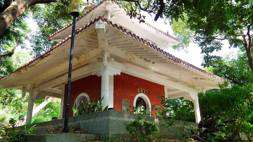 A traditional red and white pavilion with a tiled roof, surrounded by lush greenery and trees.