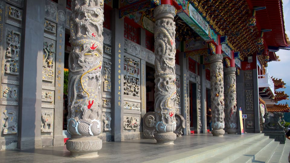 Intricately carved stone columns with traditional Chinese motifs, a red-roofed building with ornate decorations, and a clear sky.