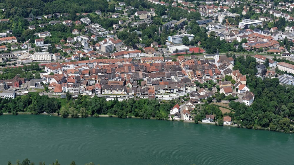 A river flowing through a densely populated town with historic buildings and a mix of residential and commercial structures.