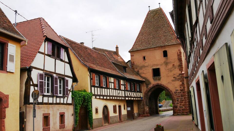 A narrow street with half-timbered houses and a stone tower.
