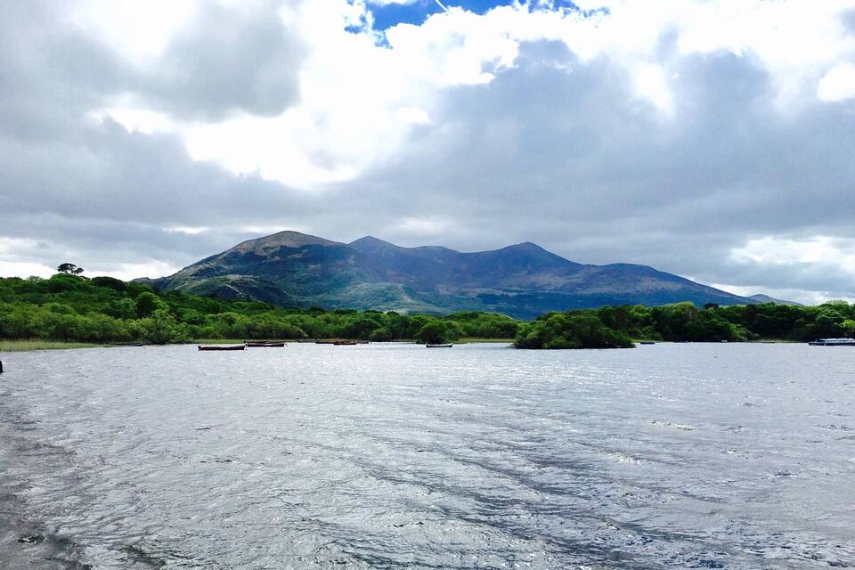 A lake with boats, surrounded by lush greenery and mountains under a cloudy sky.