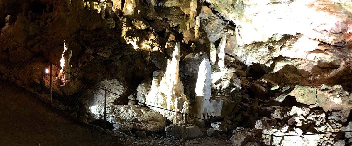 A cave with stalactites and stalagmites, a rope ladder, and a fenced area.