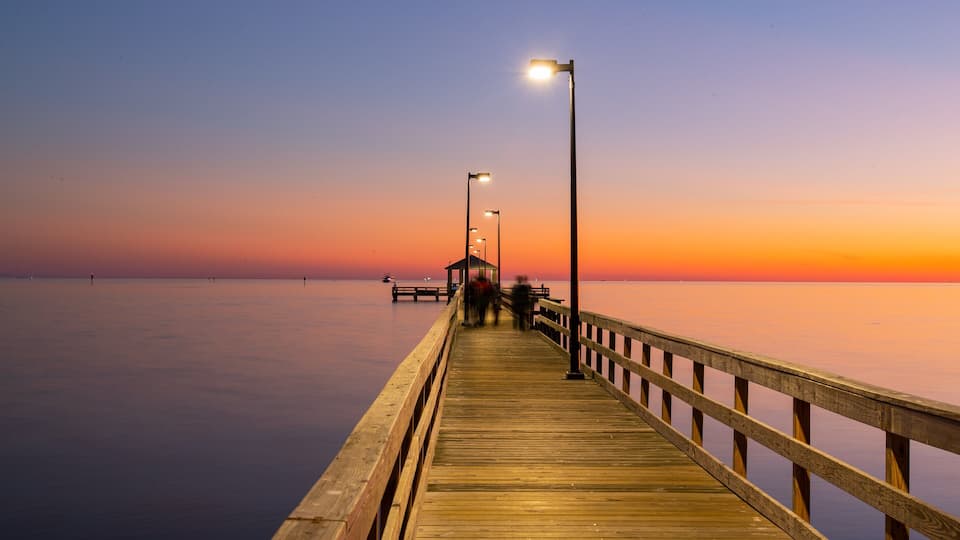 A wooden pier extending into calm waters at sunset.