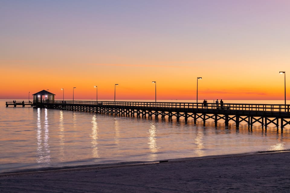 Un muelle se adentra en aguas tranquilas al atardecer, con un pequeño refugio y faroles.