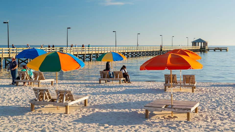 A beach with wooden chairs and colorful umbrellas, a pier extending into the water, and a lifeguard tower in the background.