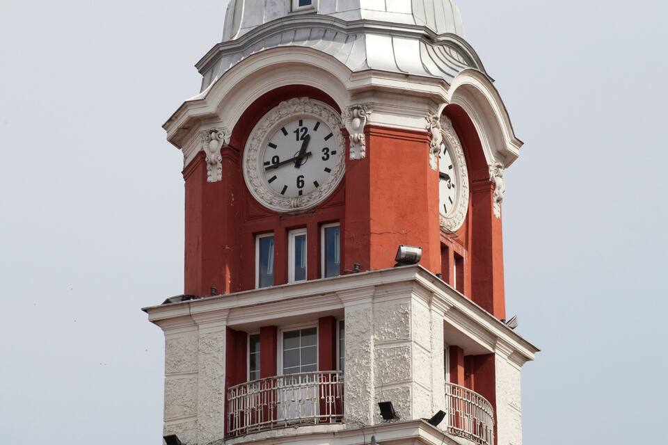 A clock tower with a red and white facade, featuring a large clock face and a dome on top.