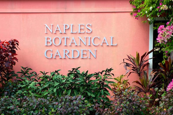 Skilt for Naples Botanisk Have med frodigt grønt og blomstrende planter omkring.