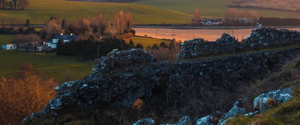 A rural landscape with rolling hills, a body of water, and a stone wall in the foreground.
