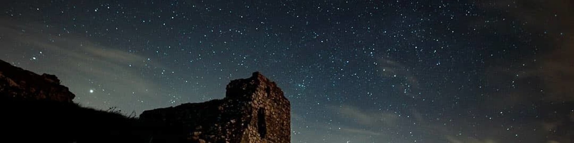 Cielo estrellado sobre un paisaje rocoso con una estructura en ruinas.