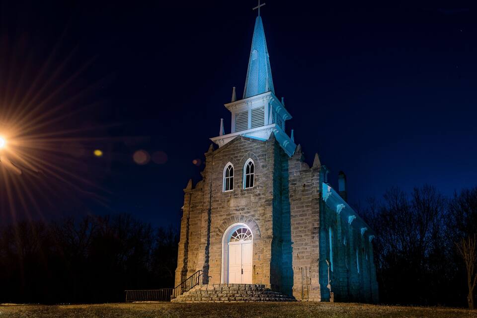 Església amb un campanar i una creu al capdamunt, il·luminada de nit.