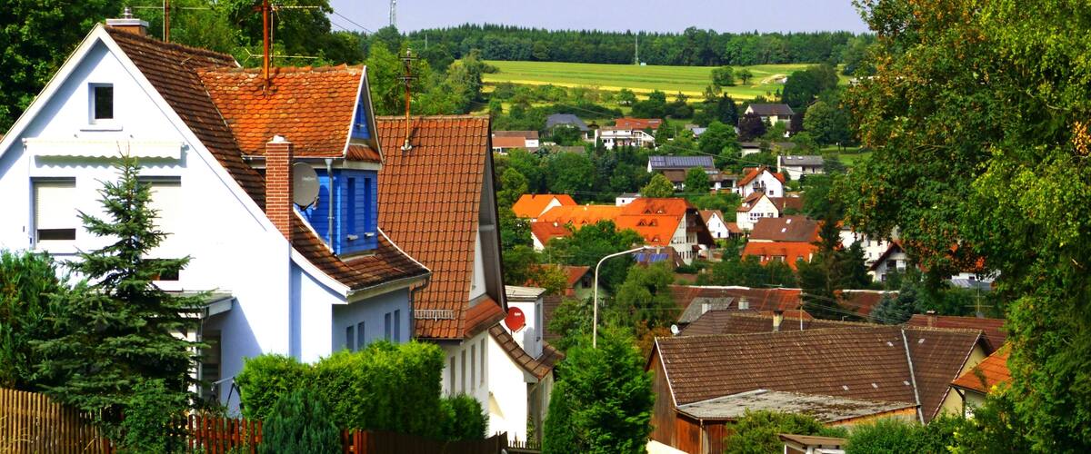 A rural village with white and red houses, a winding road, and green fields in the background.