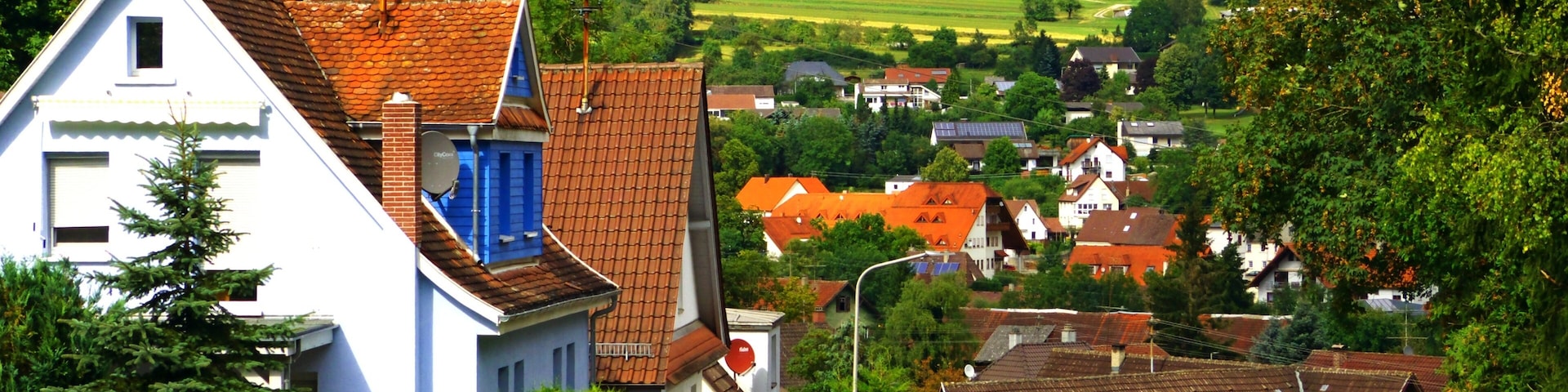 A rural village with white and red houses, a winding road, and green fields in the background.