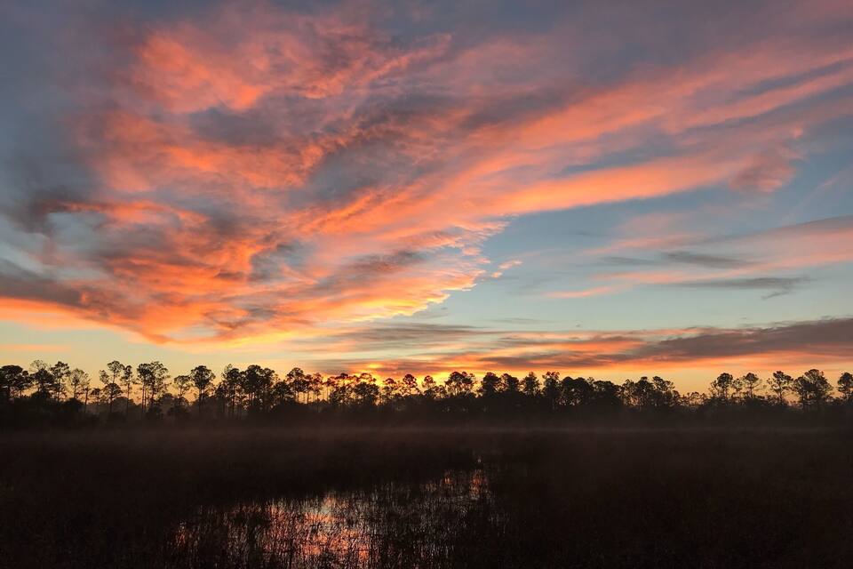 A sunset over a forest with a lake reflecting the sky.
