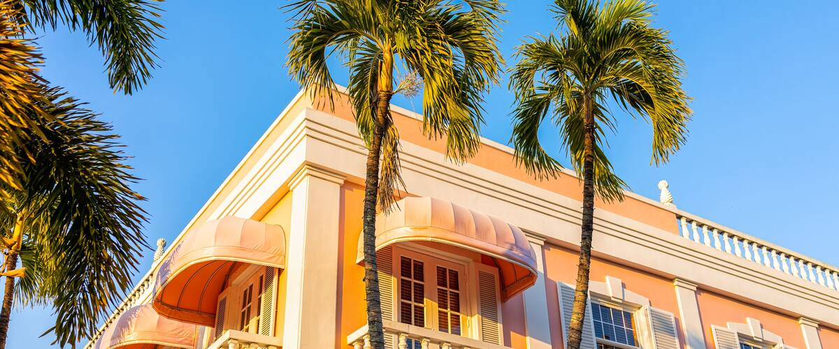 A pink building with white balconies and palm trees.