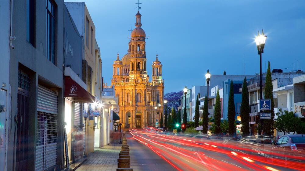Eine historische Kathedrale mit einer großen Kuppel und Glockentürmen, umgeben von modernen Gebäuden und einer belebten Straße mit Lichtspuren von Fahrzeugen.