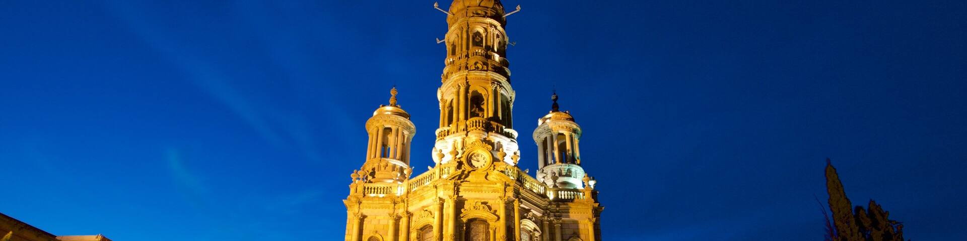 Una catedral imponente con múltiples cúpulas y una alta torre central, iluminada al anochecer.