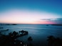 A sunset over a calm sea with a pier and palm trees.