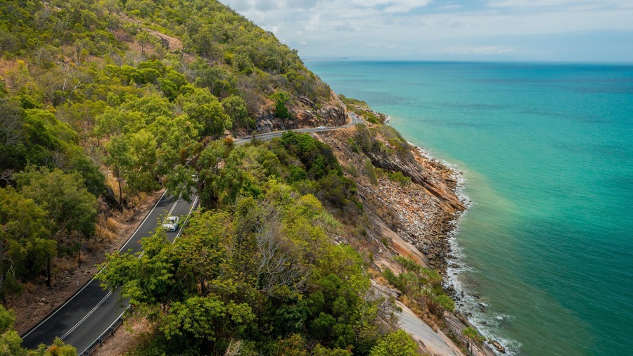 A coastal road winding through a forested hillside with a view of the ocean.
