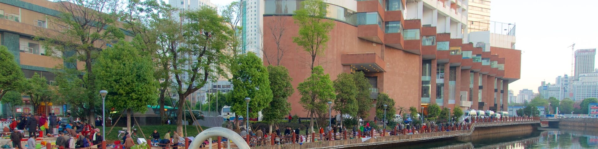 A riverside walkway with people, a bridge, and modern buildings in the background.