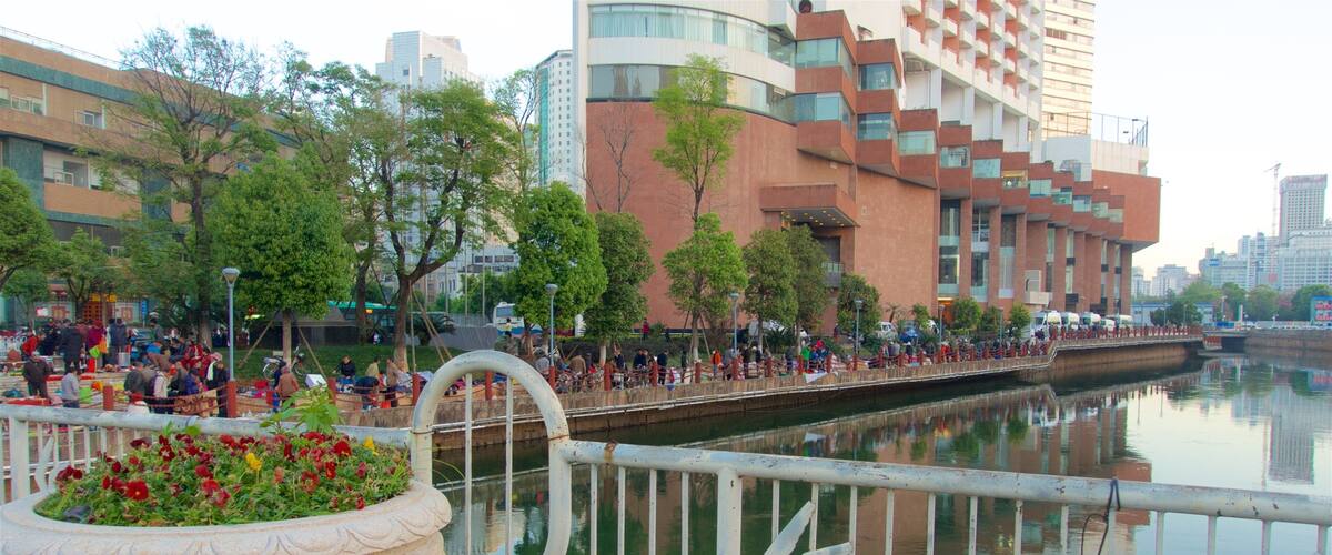 A riverside walkway with people, a bridge, and modern buildings in the background.
