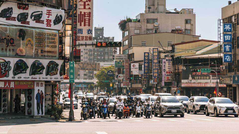 Una calle urbana concurrida, con diversas tiendas, motocicletas y automóviles.