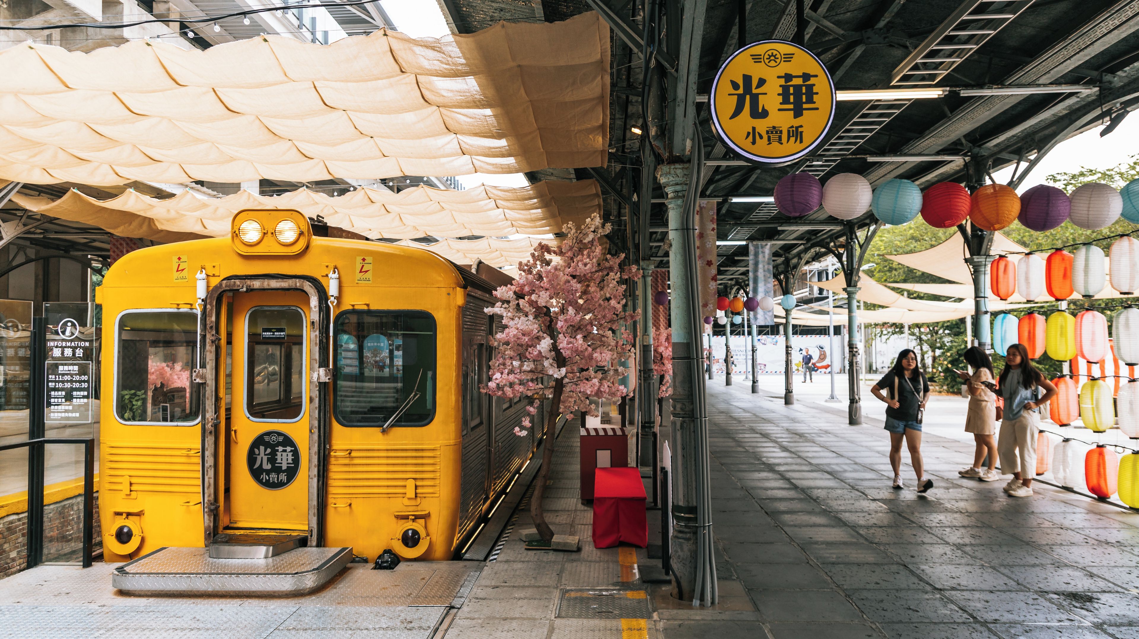 A yellow train at a station with a covered waiting area and colorful lanterns.