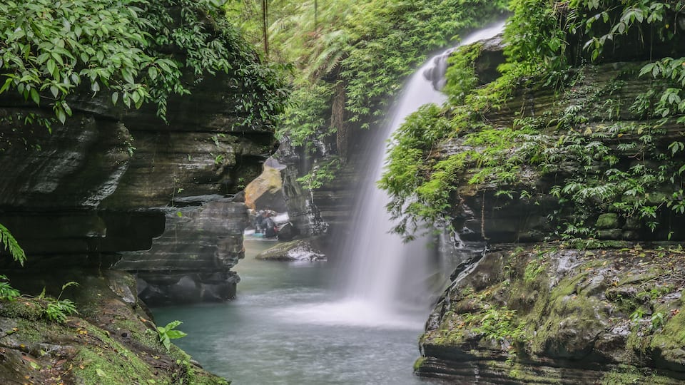 A waterfall cascading over moss-covered rocks in a lush forest.