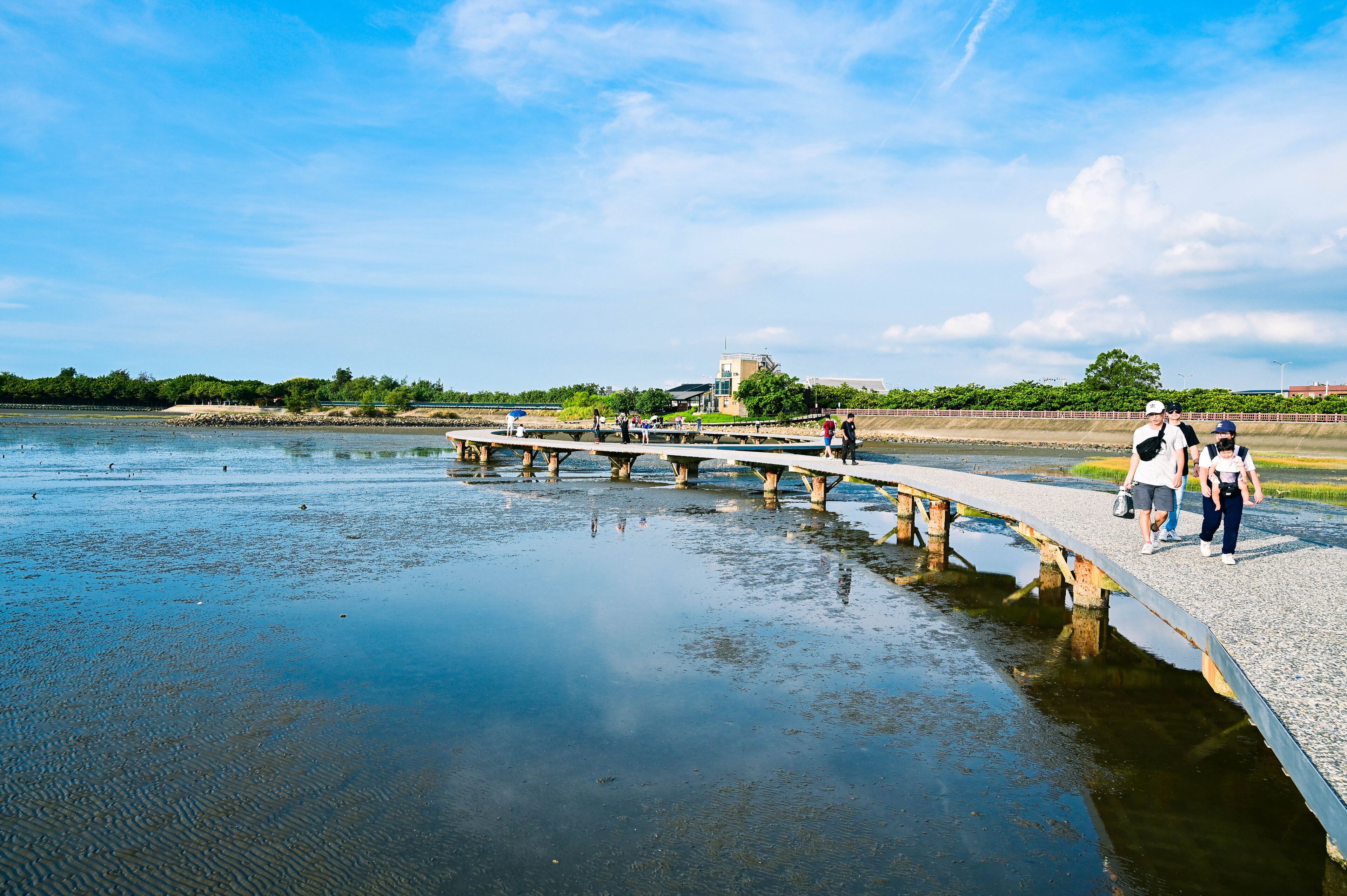 Een rivier met een betonnen brug, mensen wandelen en een gebouw op de achtergrond.