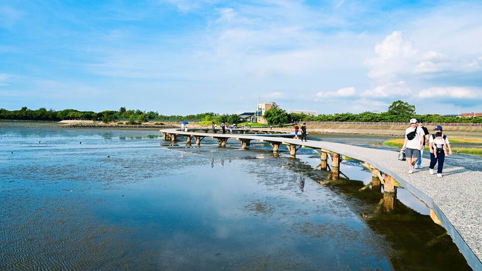 A river with a concrete bridge, people walking, and a building in the background.