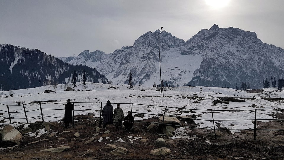 A snowy mountain landscape with a fence and people standing in the foreground.