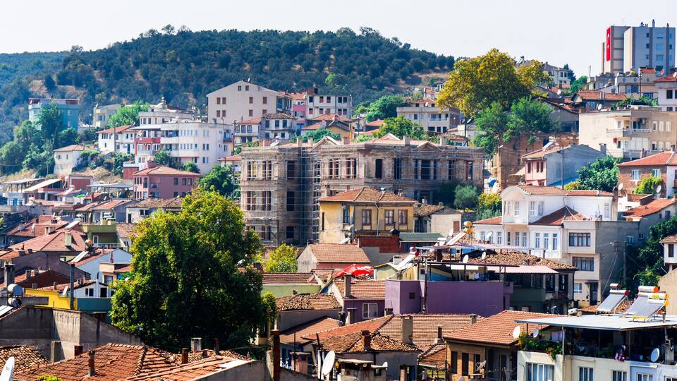 A densely packed urban area with a variety of buildings, including residential and commercial structures, and a hillside in the background.