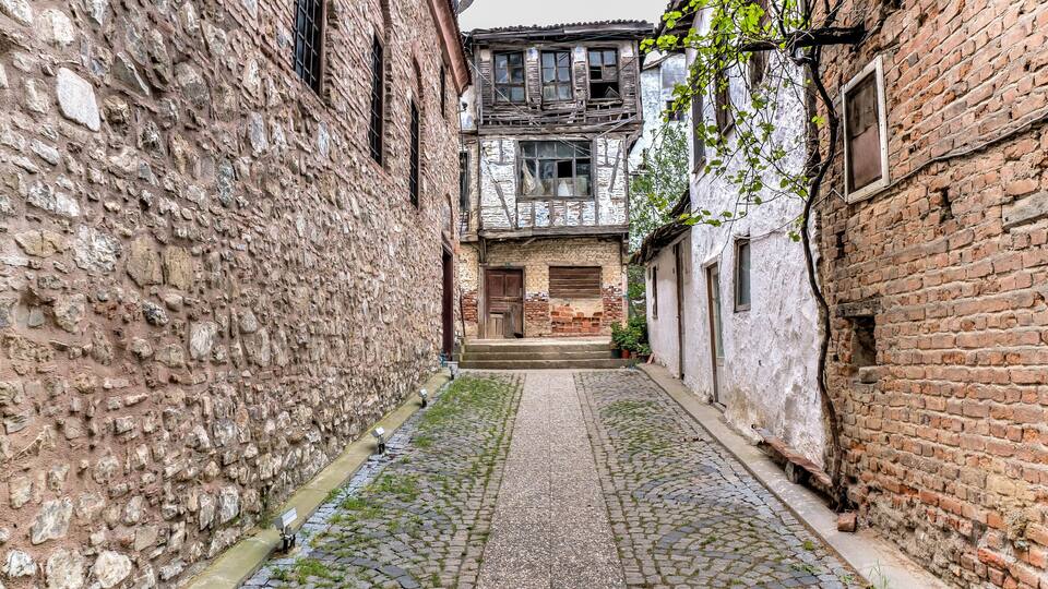 A narrow cobblestone alley flanked by old stone buildings with wooden shutters and a rustic atmosphere.