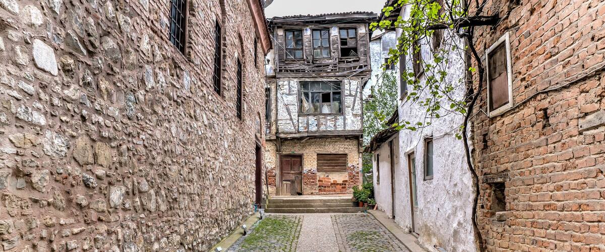 A narrow cobblestone alley flanked by old stone buildings with wooden shutters and a rustic atmosphere.
