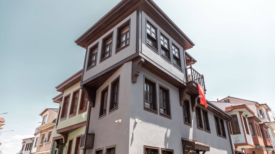 A multi-story building with a corner design, featuring large windows and a balcony with a red flag.