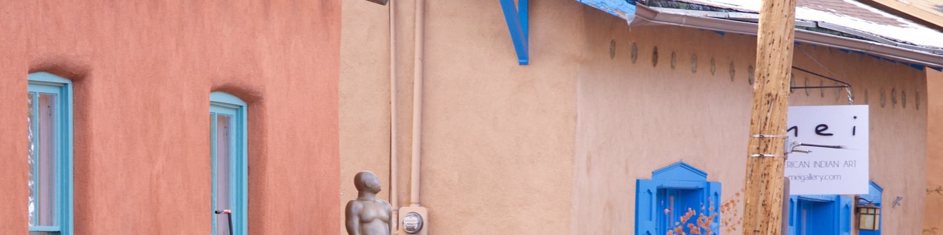A sculpture of a man and a woman on a pedestal in front of a building with blue shutters and a sign that reads "American Indian Art".