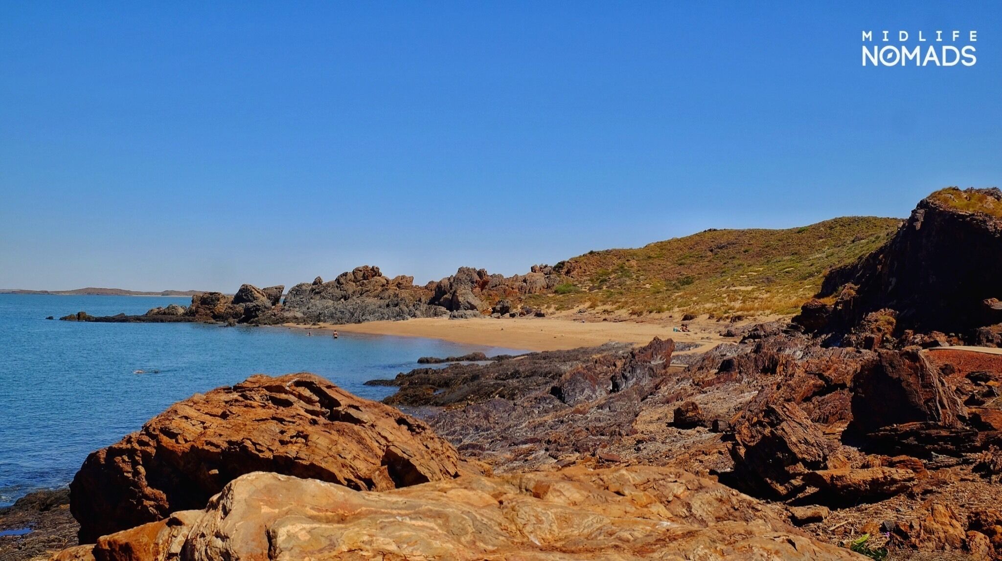 A rocky coastline with a sandy beach and clear blue sea.
