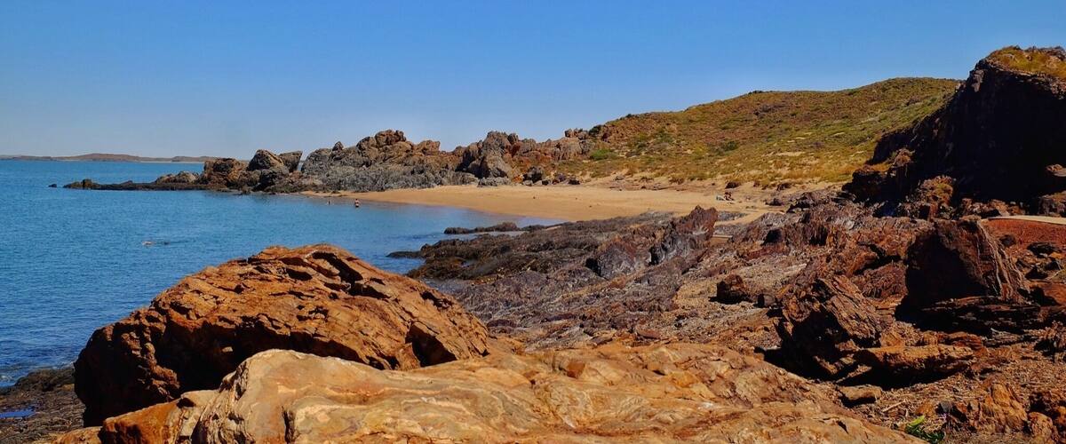 A rocky coastline with a sandy beach and clear blue sea.