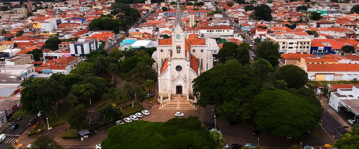 A cityscape with a prominent church featuring a clock tower, surrounded by red-roofed buildings and lush green trees.