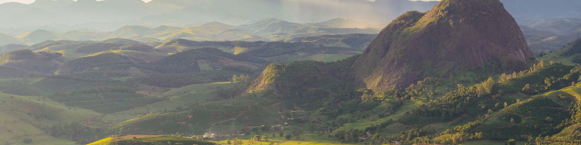 Un paisaje montañoso con campos en terrazas y un pico rocoso destacado.