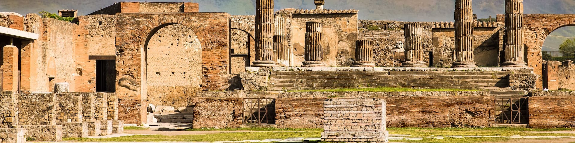 Ancient ruins with columns and arches, set against a backdrop of a mountain.