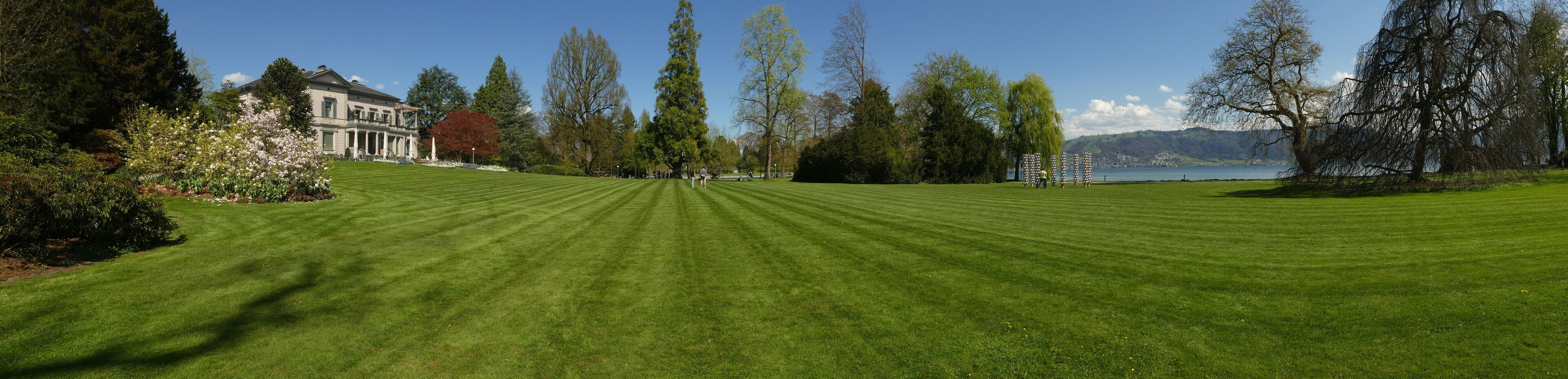 A well-manicured lawn, a large building, and a lake with mountains in the background.