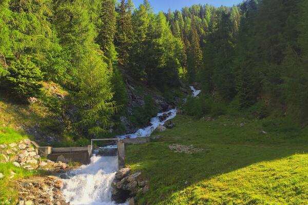 Une cascade située dans une zone boisée, avec un petit pont enjambant l’eau.