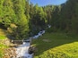 Ein Wasserfall in bewaldeter Landschaft mit einer kleinen Brücke über dem Wasser.